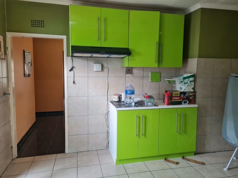 A compact kitchen area featuring bright green cabinetry, a tiled backsplash, and an integrated extractor fan, requiring minor repairs to finishes.