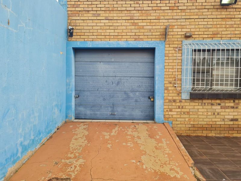 Exterior view of a single garage featuring a blue roll-up door, brick facade, and security gate, with a weathered concrete driveway.