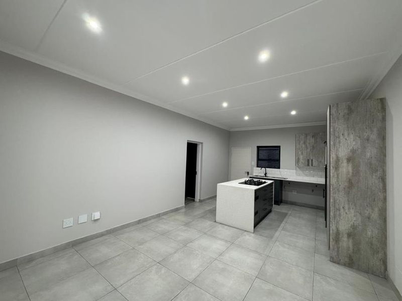 Modern open-plan kitchen featuring a central island with a gas hob, sleek cabinetry, tiled flooring, and recessed lighting in a clean, contemporary space.