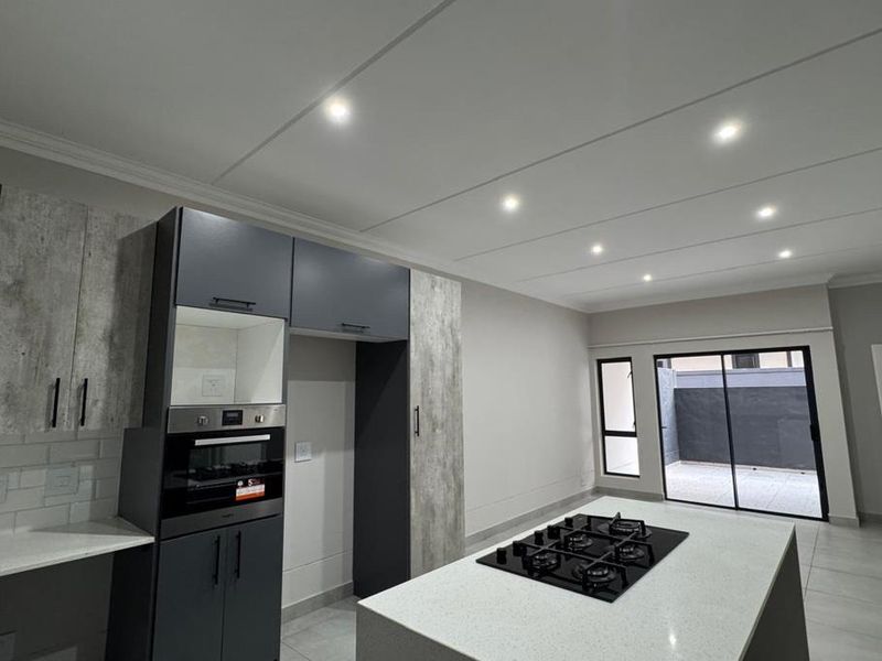 Modern kitchen featuring a central island with a gas hob, built-in oven, stone countertops, and sleek cabinetry, leading to an outdoor patio area.