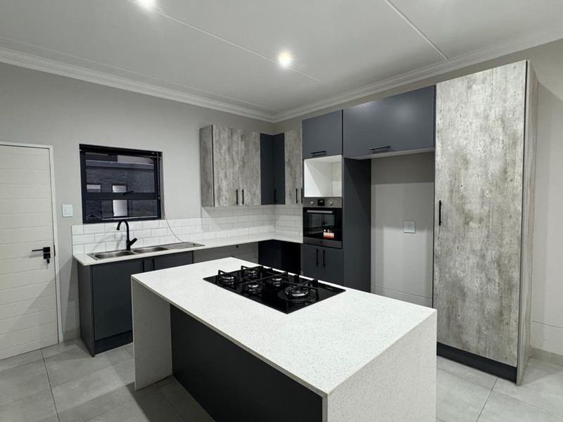 Modern kitchen featuring a central island with a gas hob, built-in oven, stone countertops, and contemporary two-tone cabinetry with a subway tile backsplash.