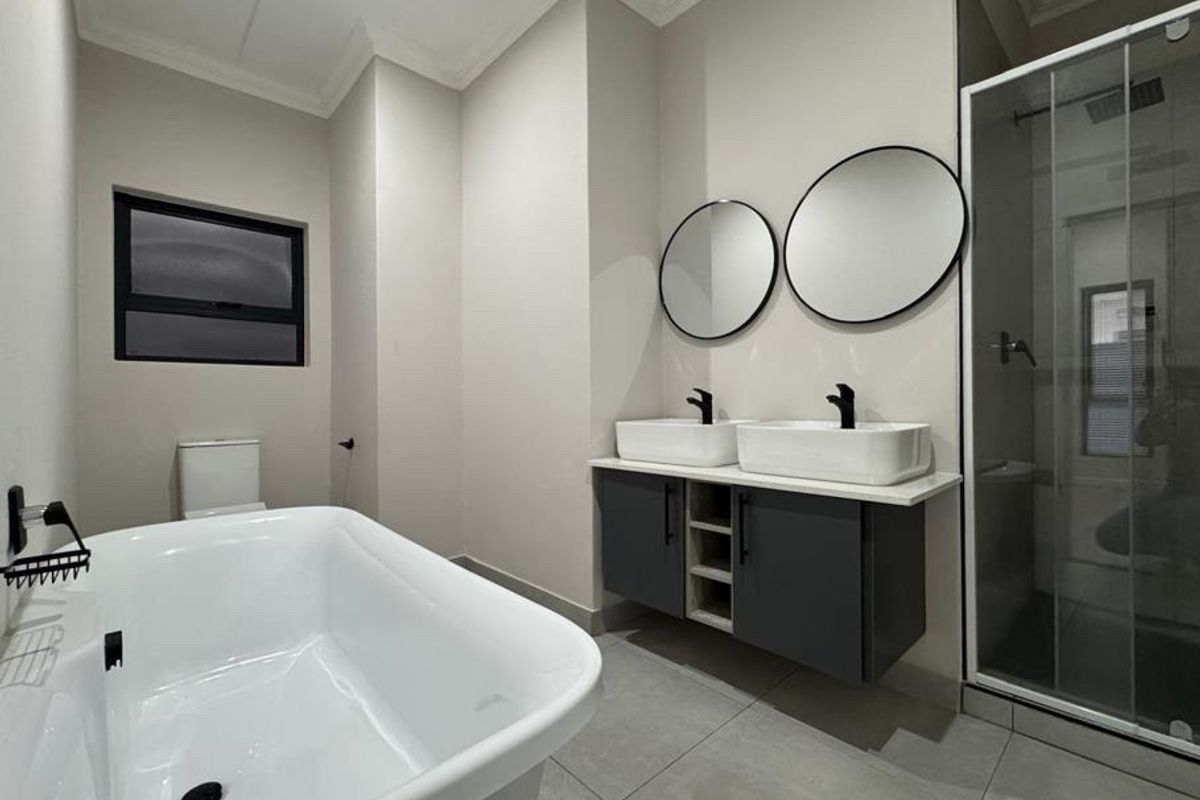 Modern bathroom featuring a freestanding bathtub, double vessel sink vanity with dark cabinetry, and a separate glass-enclosed shower.