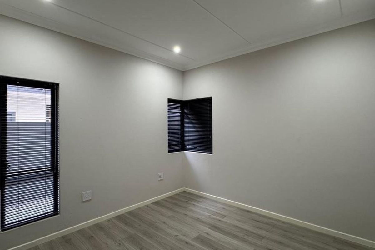 A bright, modern, and empty bedroom featuring neutral walls, laminate flooring, and recessed downlighting with fitted venetian blinds.