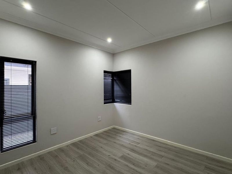A bright, modern, and empty bedroom featuring neutral walls, laminate flooring, and recessed downlighting with fitted venetian blinds.