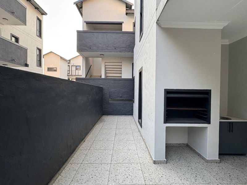 A modern covered patio area featuring a built-in braai, tiled flooring, and a convenient outdoor sink, perfect for outdoor entertaining.