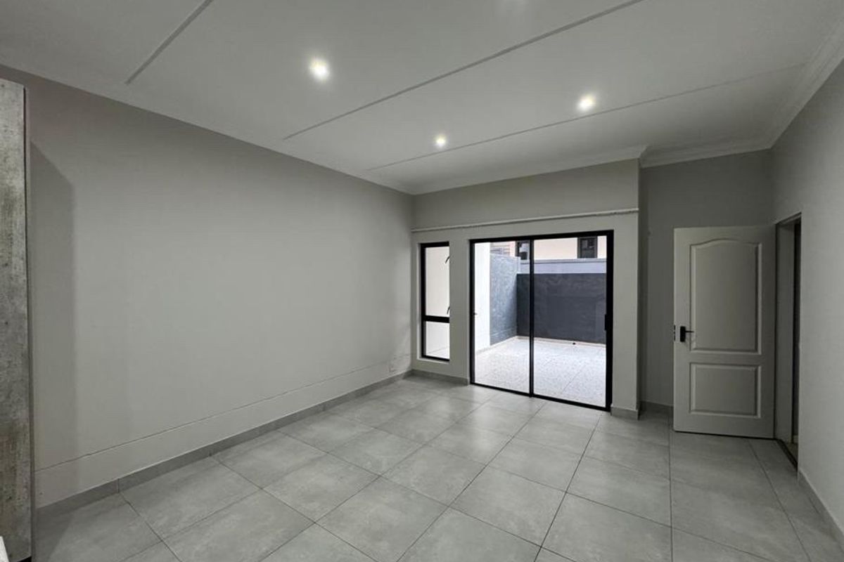 A bright, empty living room featuring modern tiled flooring, recessed downlighting, and a sliding glass door providing access to an outdoor patio area.