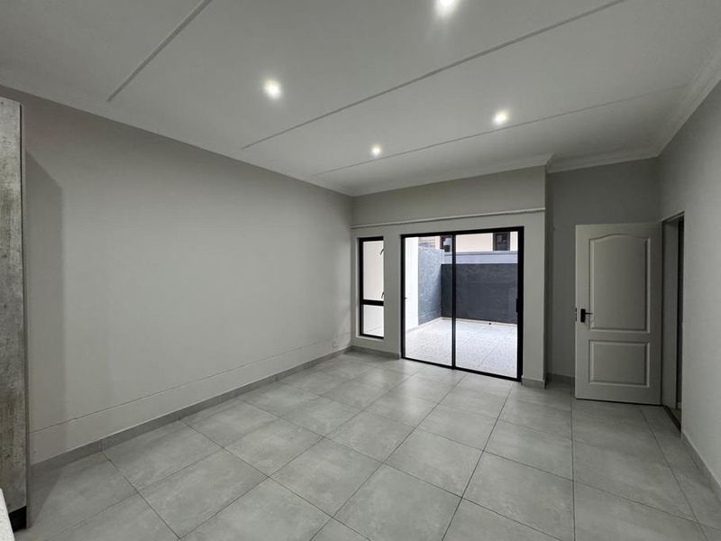 A bright, empty living room featuring modern tiled flooring, recessed downlighting, and a sliding glass door providing access to an outdoor patio area.
