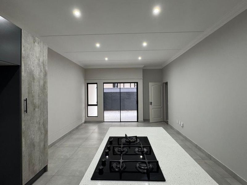 Modern open-plan kitchen and living area featuring a central island with a gas hob, sleek cabinetry, tiled floors, and direct access to an outdoor patio.