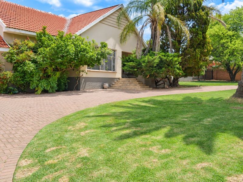 Front view of a residential house featuring a paved driveway, landscaped garden, and terracotta roof tiles.