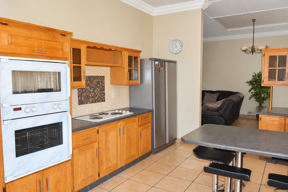 A functional kitchen featuring wooden cabinetry, built-in oven, electric hob, and tiled flooring, with an open-plan layout leading into the adjacent living area.