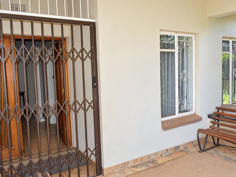 A covered patio area featuring tiled flooring, security gates, and windows with decorative security bars.