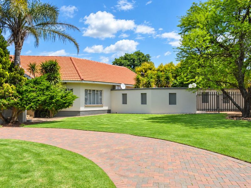 A well-maintained front exterior featuring a paved driveway, manicured lawn, and a classic tiled roof home with secure perimeter fencing.