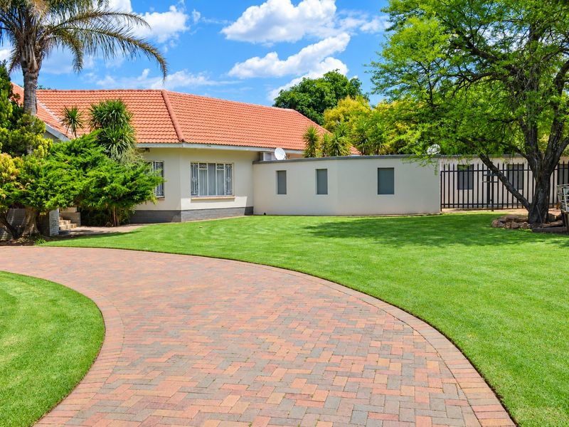 A well-maintained front exterior featuring a paved driveway, lush green lawn, and a classic house with terracotta roof tiles.