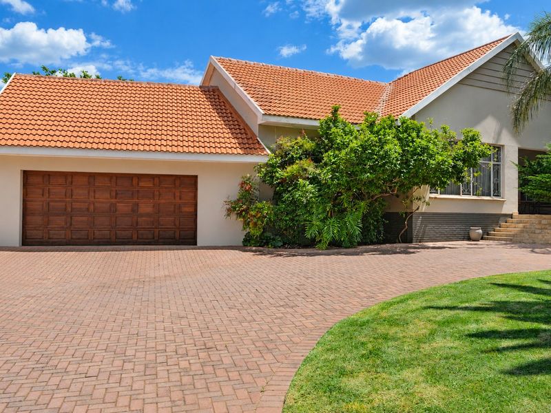 Front elevation of a well-maintained house featuring a paved driveway, a wooden garage door, and a classic tiled roof.