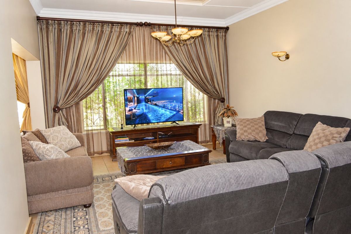 A comfortable living room featuring tiled flooring, crown molding, and decorative lighting, with large windows fitted with security bars.