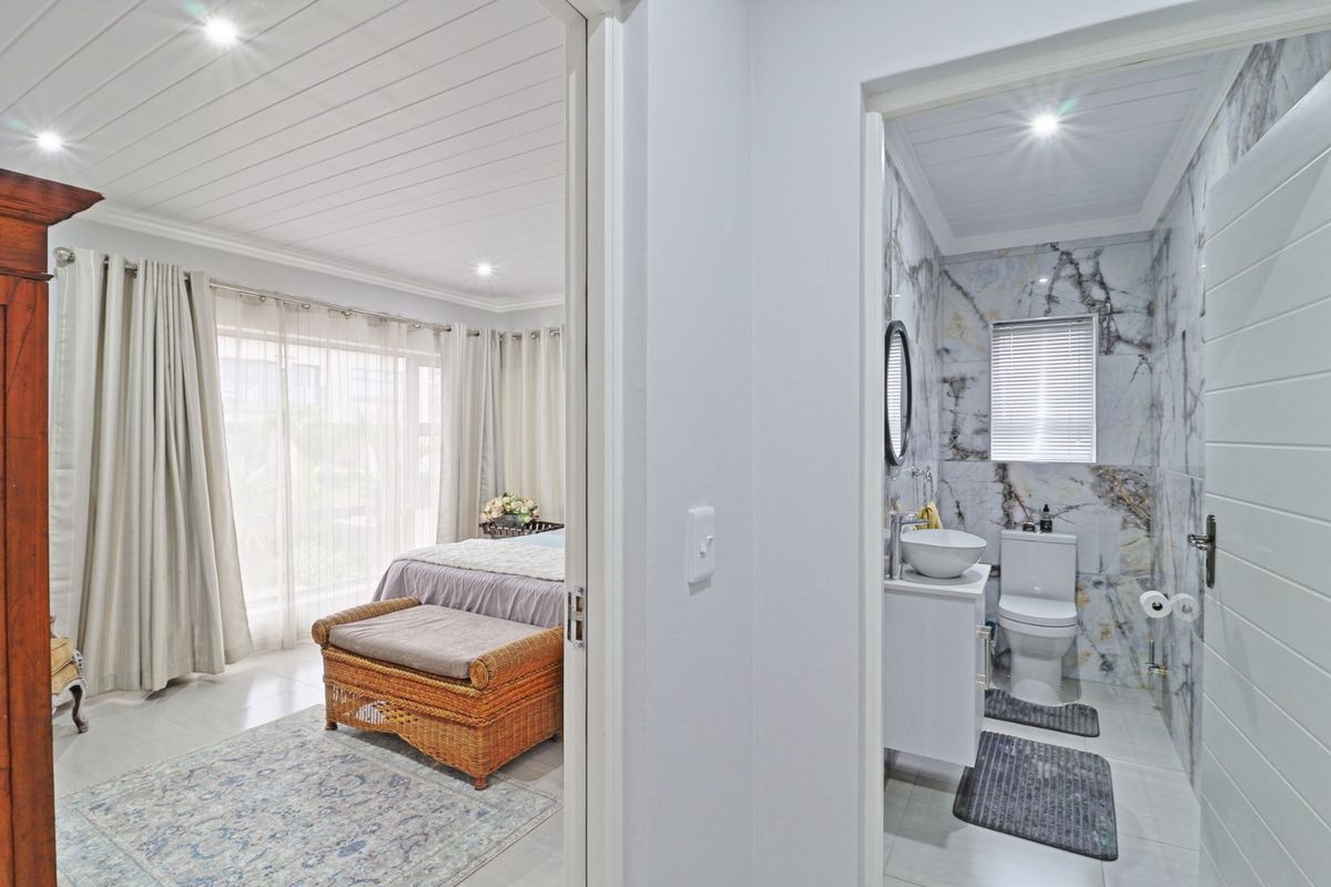 A well-maintained bedroom featuring a tongue and groove ceiling and recessed lighting, with an adjacent en-suite bathroom finished in elegant marble-look wall tiles.