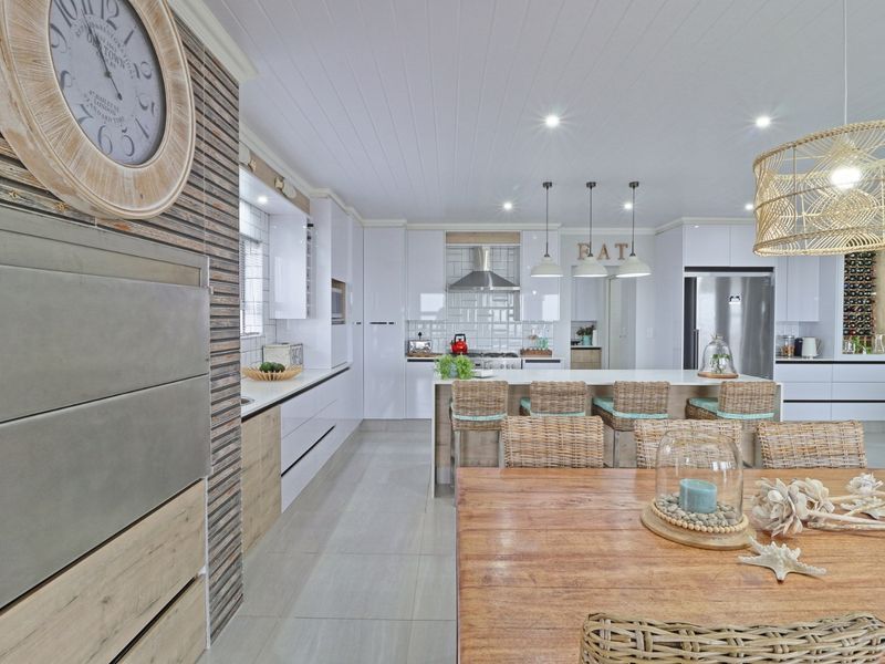 Modern open-plan kitchen featuring white gloss cabinetry, stone countertops, a central island, and stylish subway tile backsplash, seamlessly integrated with the dining area.