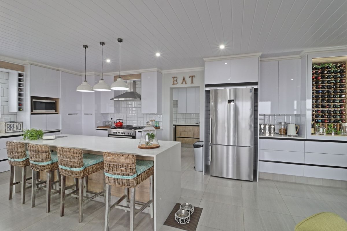 Modern kitchen featuring a large central island, sleek white cabinetry, subway tile backsplash, integrated wine storage, and high-end stainless steel appliances.