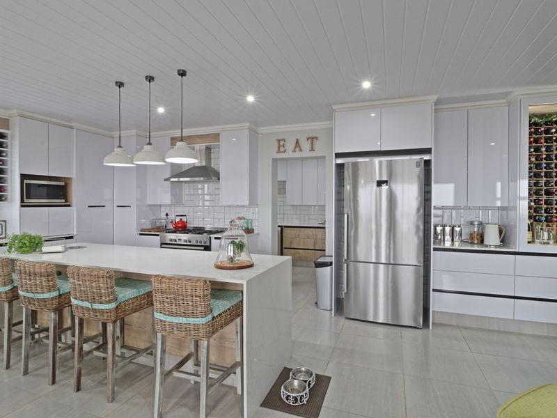 Modern kitchen featuring a large central island, sleek white cabinetry, subway tile backsplash, integrated wine storage, and high-end stainless steel appliances.