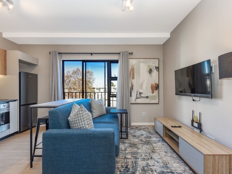 Modern open-plan living area featuring a compact kitchen with built-in appliances and a sliding door leading to a balcony.