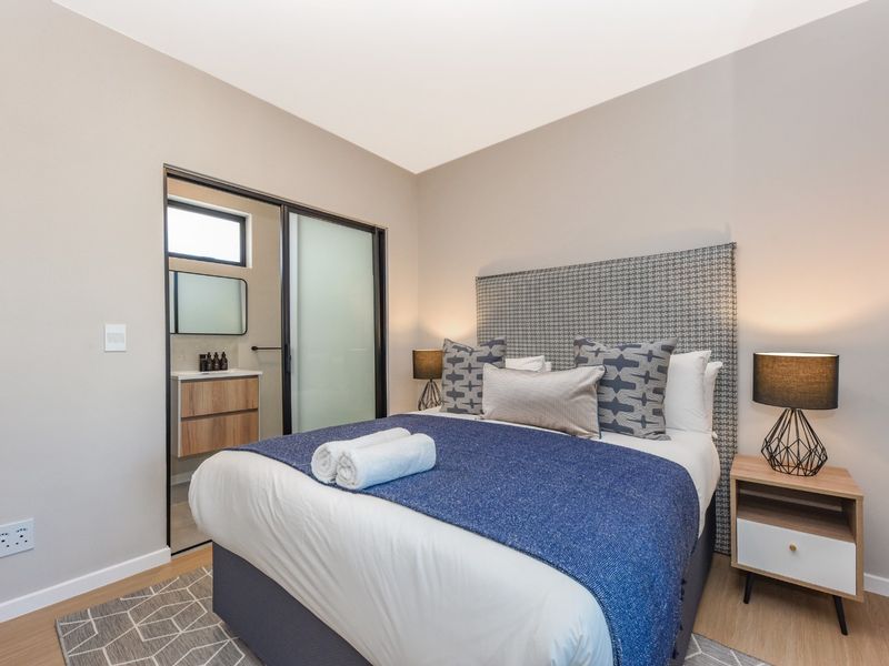 A modern, well-maintained bedroom featuring laminate flooring, neutral walls, and an en-suite bathroom accessible via a sliding door.