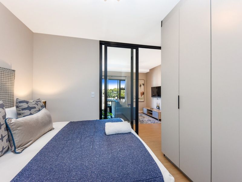 Modern bedroom featuring sleek built-in wardrobes, laminate flooring, and a stylish sliding glass door providing a view into the adjacent living area.