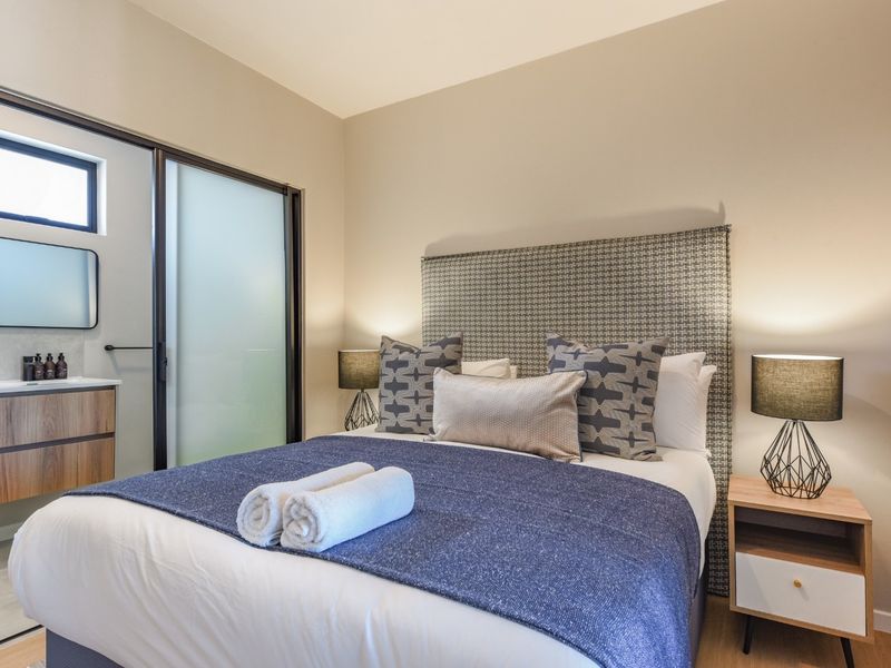 A well-appointed bedroom featuring an integrated en-suite bathroom with a modern vanity and sliding glass door access.