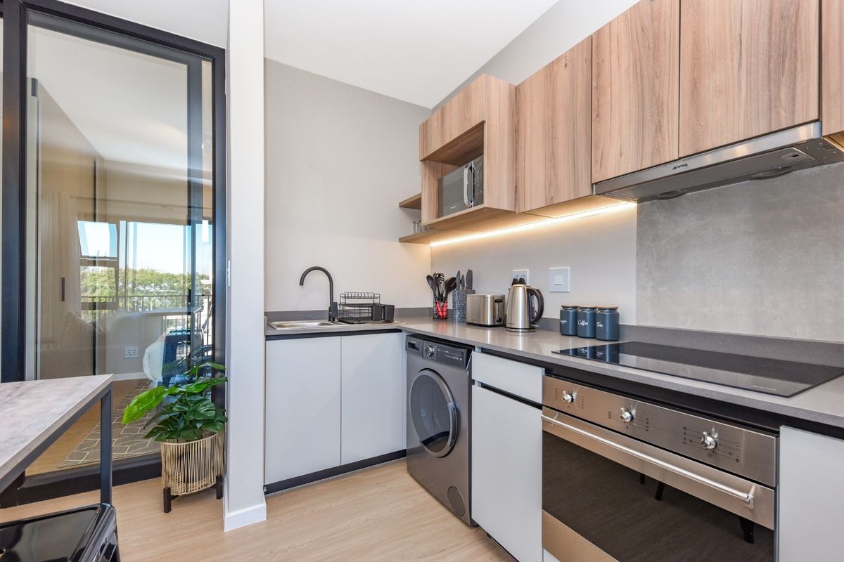 Modern kitchen featuring sleek cabinetry, stone countertops, integrated appliances including an oven and hob, and under-cabinet lighting, adjacent to a glass balcony door.
