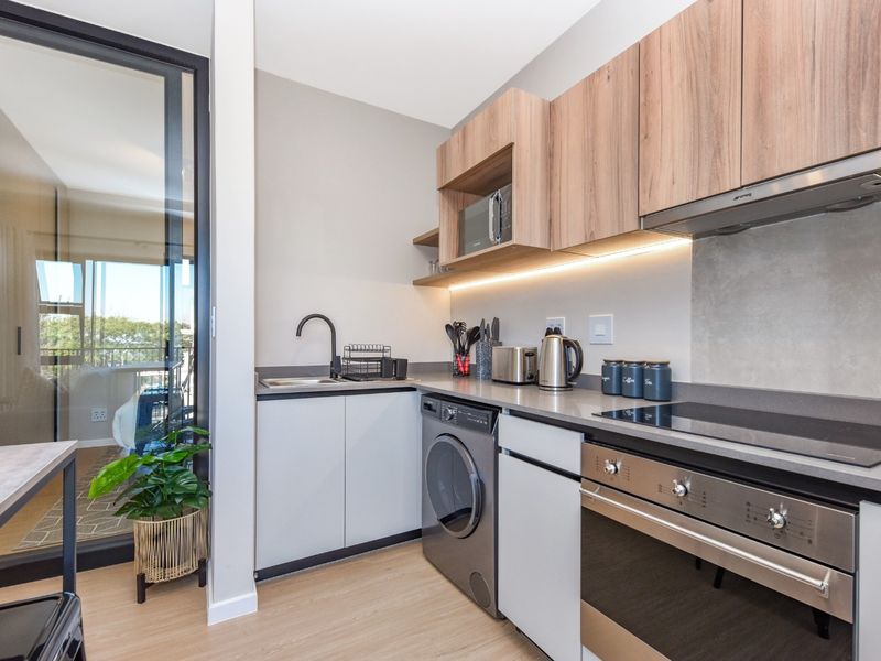 Modern kitchen featuring sleek cabinetry, stone countertops, integrated appliances including an oven and hob, and under-cabinet lighting, adjacent to a glass balcony door.