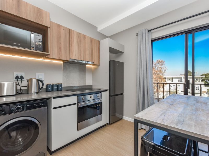 Modern open-plan kitchen featuring sleek cabinetry, integrated appliances, and direct access to a balcony with neighborhood views.
