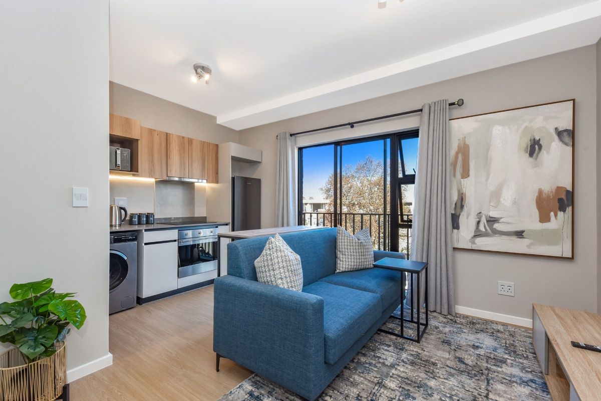 Modern open-plan apartment featuring a compact kitchen with built-in appliances and a living area with direct access to a balcony through sliding doors.