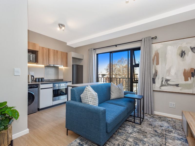 Modern open-plan apartment featuring a compact kitchen with built-in appliances and a living area with direct access to a balcony through sliding doors.