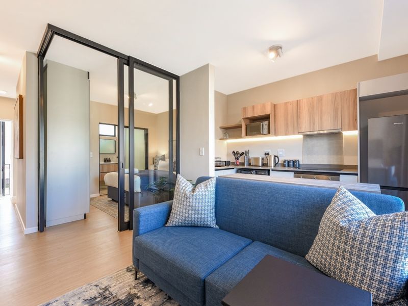 Modern open-plan apartment featuring a sleek kitchen with wood-finish cabinetry and a stylish glass sliding partition separating the living area from the bedroom.