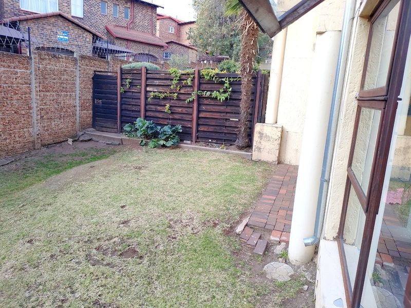 A private rear garden area featuring a small lawn, paved walkway, and timber boundary fencing, providing a compact outdoor space for the townhouse.