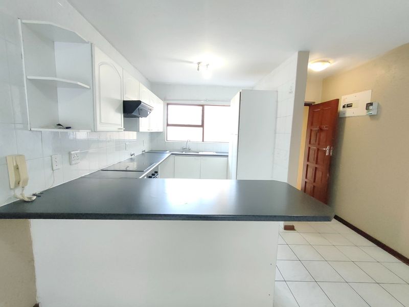 A functional, empty kitchen featuring white cabinetry, dark laminate countertops, a breakfast bar, and tiled flooring, offering a clean canvas for modern updates.