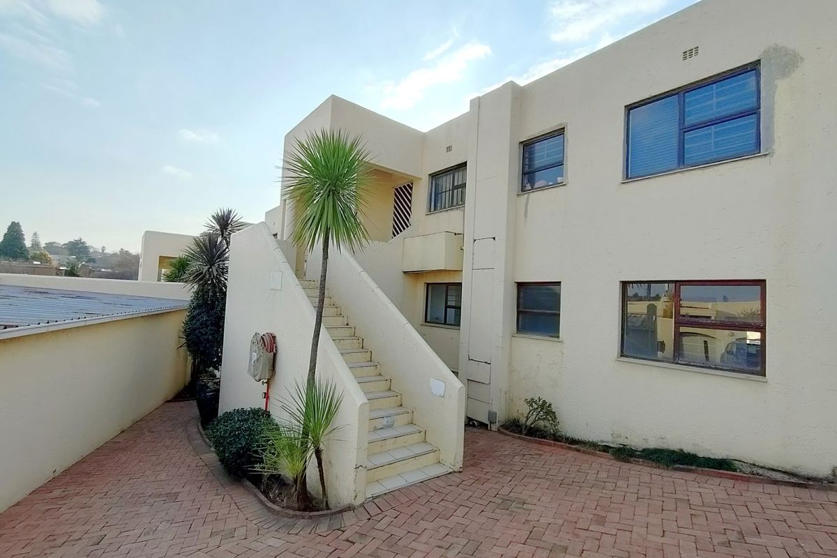 Rear exterior view of a townhouse complex featuring a paved courtyard, external staircase, and multi-level residential units with aluminium window frames.