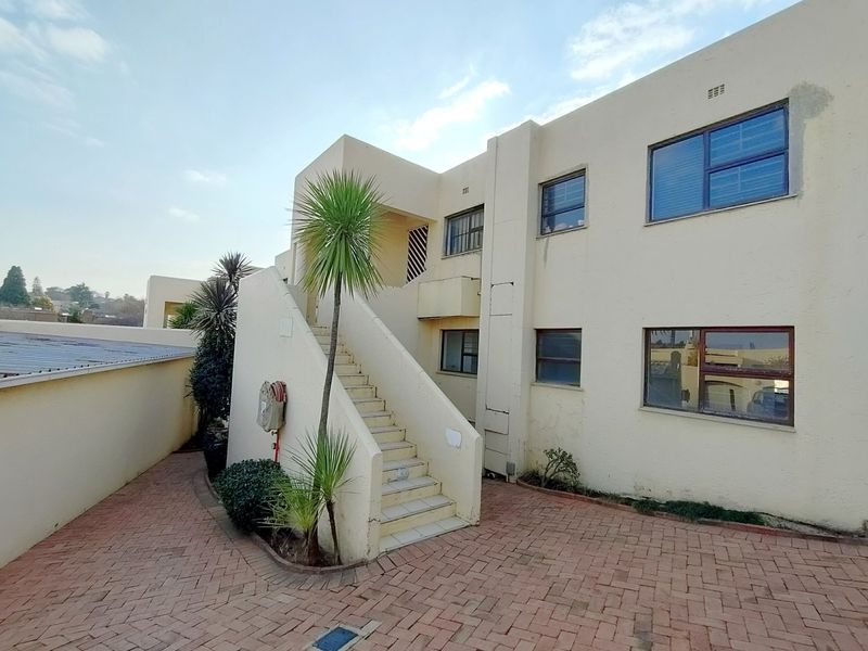 Rear exterior view of a townhouse complex featuring a paved courtyard, external staircase, and multi-level residential units with aluminium window frames.