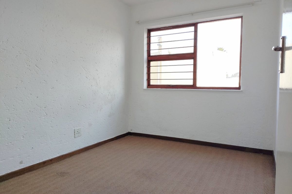 An empty bedroom featuring textured walls, carpet flooring, and a window fitted with security burglar bars.