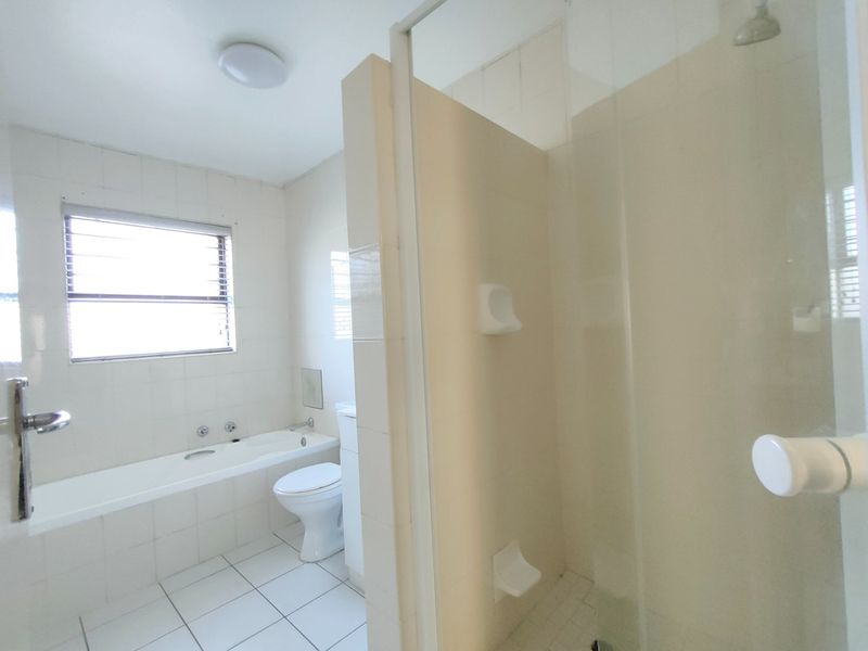 A functional bathroom featuring a built-in bathtub, separate shower enclosure, and toilet with neutral tiled finishes throughout.