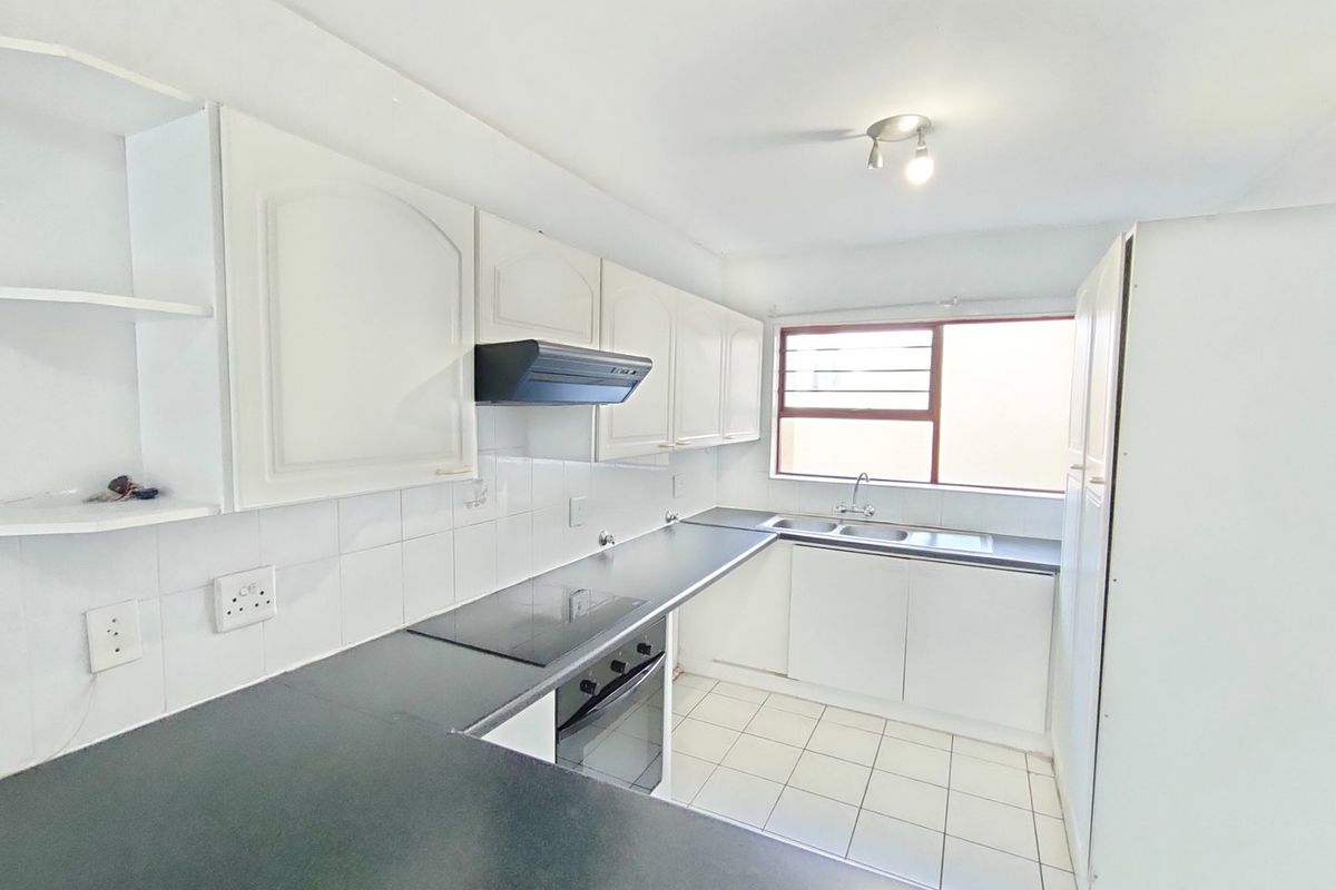 A functional kitchen featuring white cabinetry, dark laminate countertops, built-in oven and hob, and tiled flooring, offering a clean canvas for modern updates.