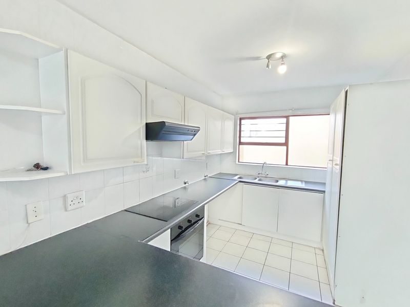 A functional kitchen featuring white cabinetry, dark laminate countertops, built-in oven and hob, and tiled flooring, offering a clean canvas for modern updates.