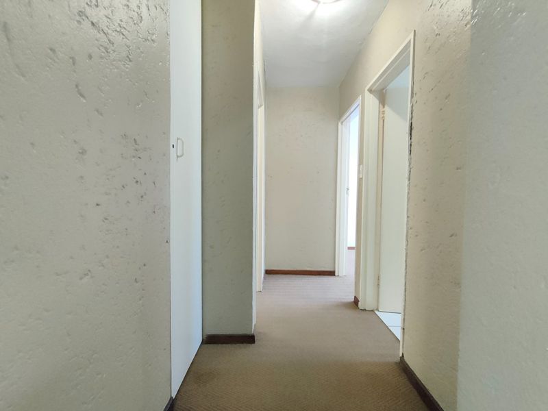 A vacant interior hallway featuring neutral walls, carpeted flooring, and built-in storage cupboards, providing access to multiple rooms within the townhouse.