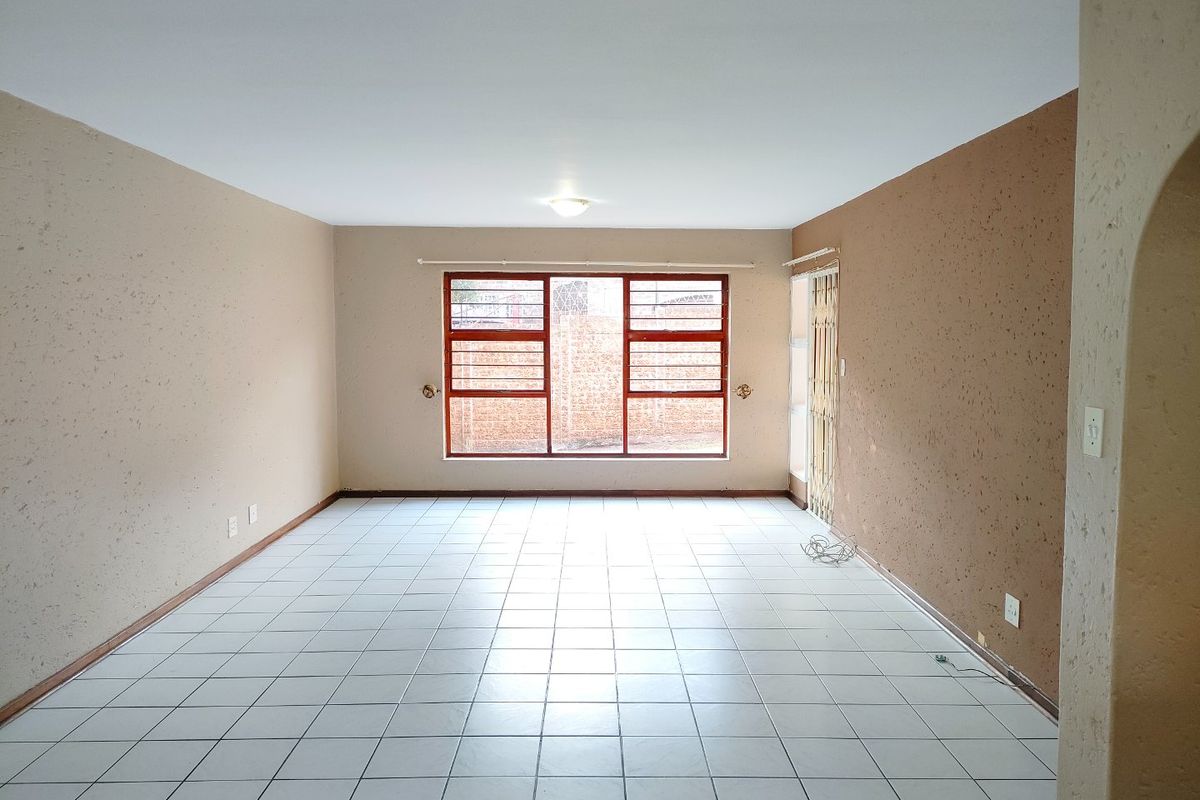 An empty, open-plan living area featuring tiled flooring, a large window with security bars, and a side security gate.