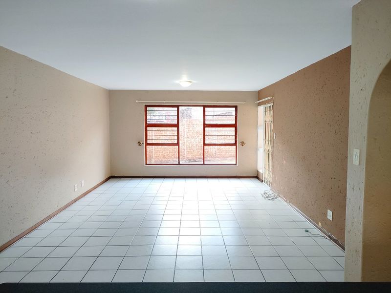 An empty, open-plan living area featuring tiled flooring, a large window with security bars, and a side security gate.