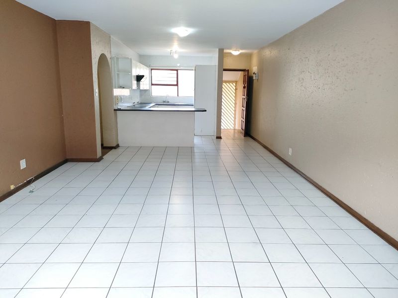 An open-plan living and kitchen area featuring tiled flooring, a breakfast bar, and neutral wall finishes, offering a blank canvas for interior design.