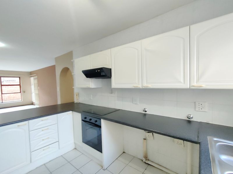 A functional kitchen featuring white cabinetry, dark countertops, built-in oven and hob, and tiled flooring, opening into an adjacent living area through an archway.
