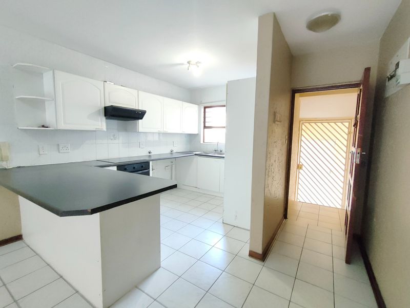 A functional kitchen featuring white cabinetry, dark laminate countertops, and tiled flooring, with an adjacent doorway leading to a secure exterior entrance.