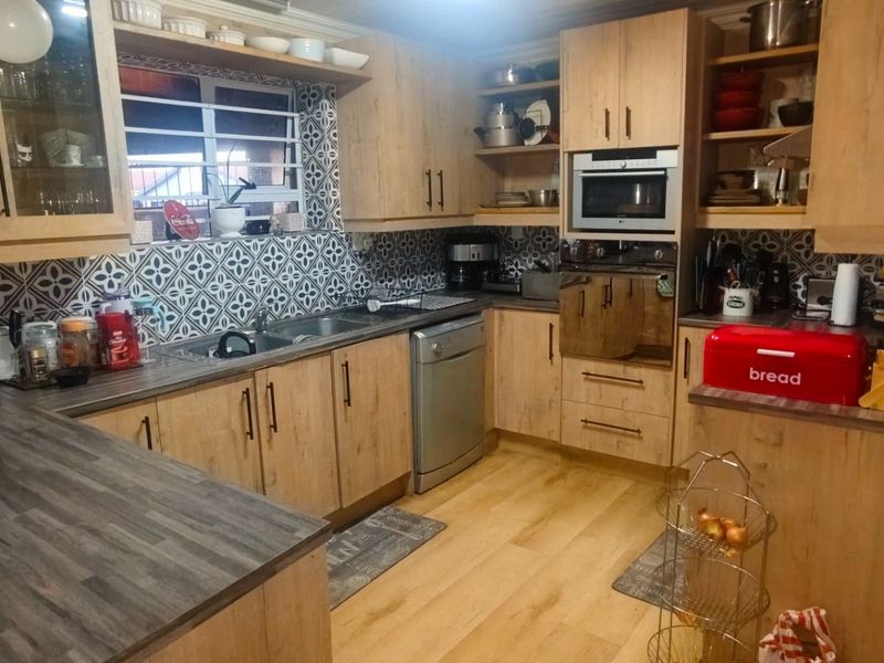 A functional kitchen featuring light wood-look cabinetry, patterned tile backsplash, integrated appliances, and durable laminate countertops with ample storage space.
