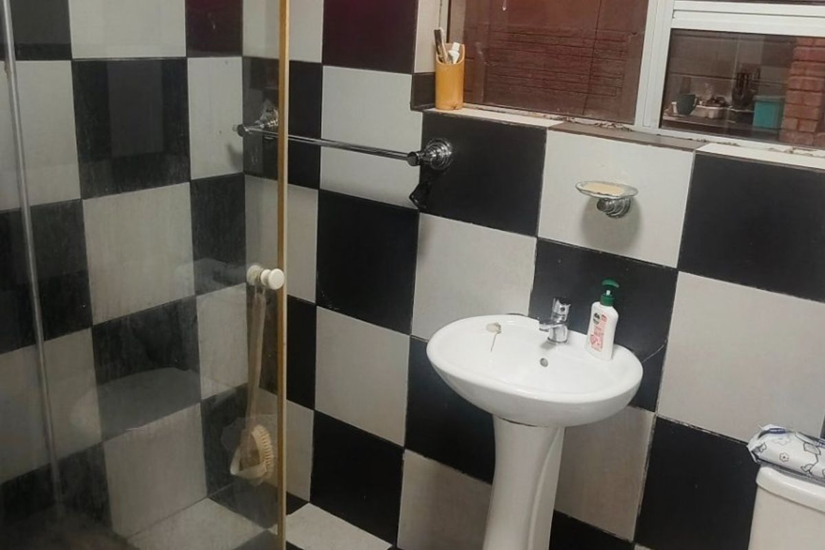A compact bathroom featuring a pedestal basin, toilet, and shower enclosure with a distinctive black and white checkered tile finish.