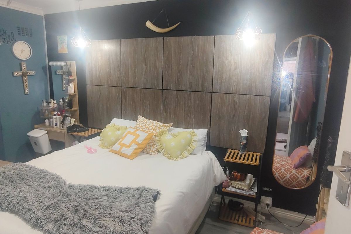 A bedroom featuring a dark accent wall with decorative wood-look paneling and modern pendant lighting.